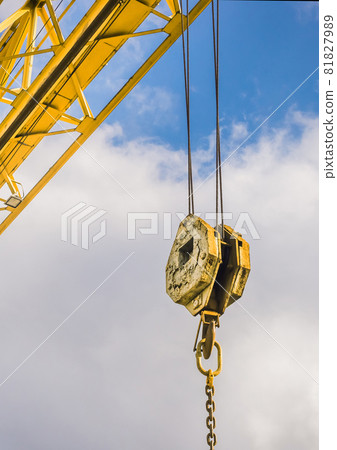 Overhead crane hoist industrial mechanism with hook and chain on a background of blue sky with clouds, close-up Overhead crane hoist industrial mechanism with hook and chain on a background of blue sky with clouds, close-up 81827989