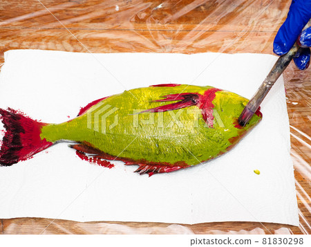 masterclass for Fish Drawing in Technique Monotype - view of gloved hand colors eye of green Orata fish with red acrylic paint on paper towel on table covered with plastic wrap 81830298