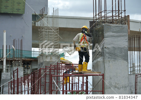 MELAKA, MALAYSIA -JULY 05, 2016: Construction workers wearing safety harness and adequate safety gear while working at high level at the construction site in Melaka, Malaysia. 81834347