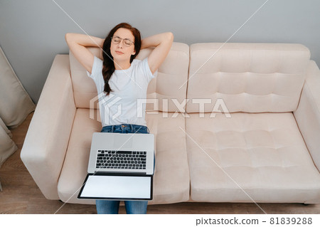 Young woman relaxes sitting on the sofa after doing work on a laptop 81839288