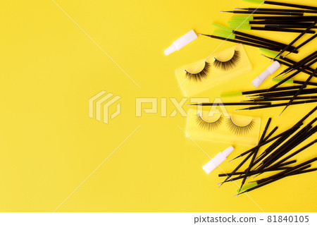 Different tools for eye lash extension on trendy bright yellow background. Fake eyelashes, brushes and clay. Beauty concept, makeup cosmetics. Place for text and design. Banner, flyer 81840105