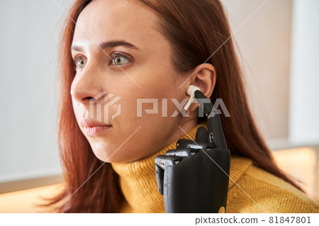 Woman with prosthesis arm listening music in headphones 81847801