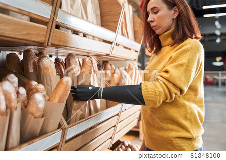 Woman with implant arm touching bread at grocery store 81848100