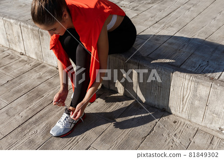High angle shot of attractive young sportswoman tying her shoelaces before workout or jogging outdoors High angle shot of attractive young sportswoman tying her shoelaces before workout or jogging outdoors 81849302
