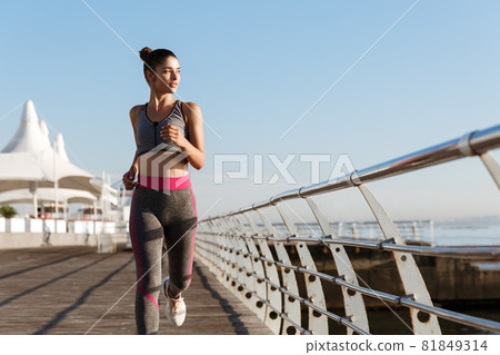 Image of fit and healthy woman jogging in the morning, looking at sea during workout. Female runner training on the seaside promenade 81849314