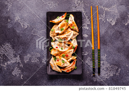 Fried dumplings served with green onions, sesame seeds and chili peppers 81849745
