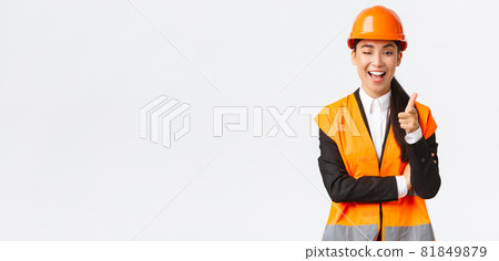 Smiling professional asian female construction manager in safety helmet and reflective jacket inviting check-out new building, wink and pointing finger at camera, showing client best estate Smiling professional asian female construction manager in safety helmet and reflective jacket inviting check-out new building, wink and pointing finger at camera, showing client best estate 81849879