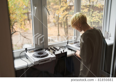 Woman standing near the window and placing her dj equipment Woman standing near the window and placing her dj equipment 81850881