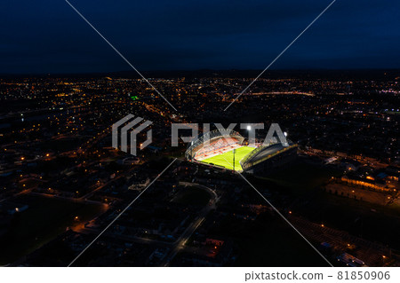 Aerial view of stadium with green grass pitch and focus lights on in Ireland surrounded by residential house in city at night 81850906