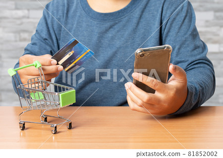 Young man holding credit card with smart phone on desk. Online shopping. 81852002