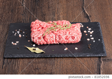 Ground beef with spices on a stone board over a wooden background. Ground beef with spices on a stone board over a wooden background. 81852036