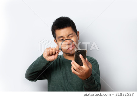 young man looking through magnifying glass at smartphone on gray background. 81852557