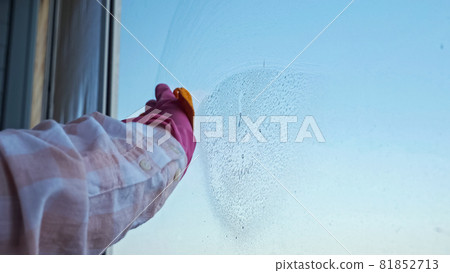 Close-up of hands in gloves cleaning the window with a rag against the background of clear sky 81852713