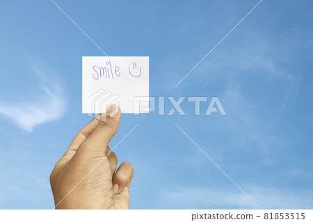 Hand holding smile word on paper card with blue sky background. Hand holding smile word on paper card with blue sky background. 81853515