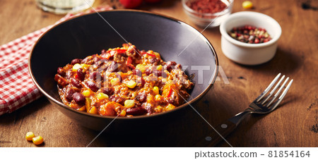 Chili Con Carne with ground beef, beans and corn in dark bowl on wooden background. Mexican and Texas cuisine Chili Con Carne with ground beef, beans and corn in dark bowl on wooden background. Mexican and Texas cuisine 81854164
