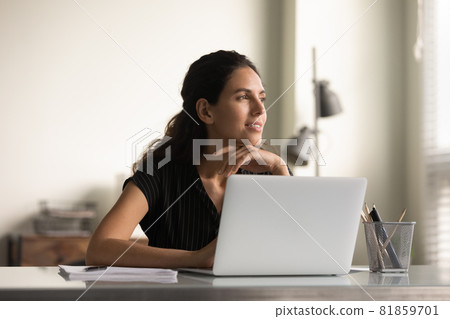 Smiling thoughtful female employee working at laptop from home Smiling thoughtful female employee working at laptop from home 81859701