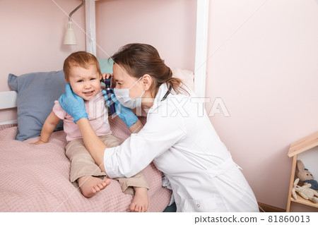 Pediatrician checking ear of baby girl with otoscope performing ENT exam at home during lockdown Pediatrician checking ear of baby girl with otoscope performing ENT exam at home during lockdown 81860013