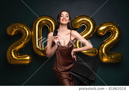 Woman in elegant dress hold credit bank card and shopping bags on black background, numbers air balloons studio. 81862018