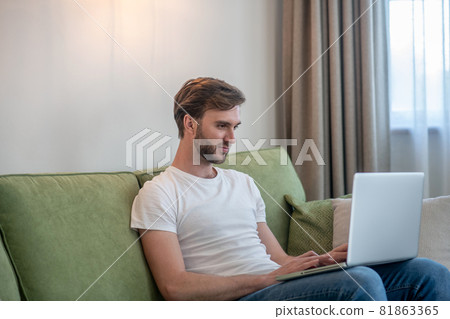 Young bearded man working on a laptop and looking involved Young bearded man working on a laptop and looking involved 81863365