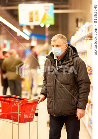 A 65-year-old man in a blue medical mask picks up groceries at a supermarket. 81863549