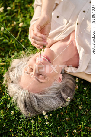 Woman with flower in hand lying on lawn Woman with flower in hand lying on lawn 81864037