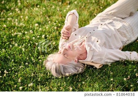 Woman lying on grass looking at flower Woman lying on grass looking at flower 81864038