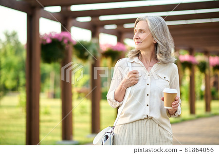 Woman with coffee looking to side in park Woman with coffee looking to side in park 81864056