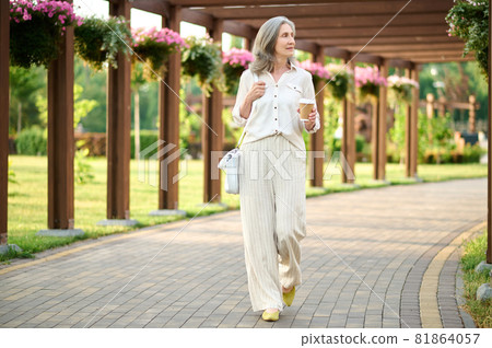 Gray-haired woman with coffee in blooming park Gray-haired woman with coffee in blooming park 81864057