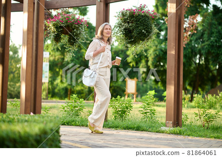Meditative woman with coffee walking in park 81864061