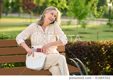 Elegant woman with smartphone putting notebook in handbag Elegant woman with smartphone putting notebook in handbag 81864302