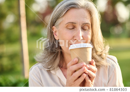 Woman with closed eyes holding glass of coffee Woman with closed eyes holding glass of coffee 81864303