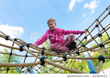 Happy child is playing in the playground. The child is sitting in a spider web 81864412