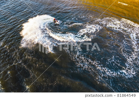 Aerial view of Young man making infinite loop riding on fast water scooter on sunset in Golden water. Drone photo of tourist having fun riding a water bike doing eight sign on the sea with pleasure Aerial view of Young man making infinite loop riding on fast water scooter on sunset in Golden water. Drone photo of tourist having fun riding a water bike doing eight sign on the sea with pleasure 81864549