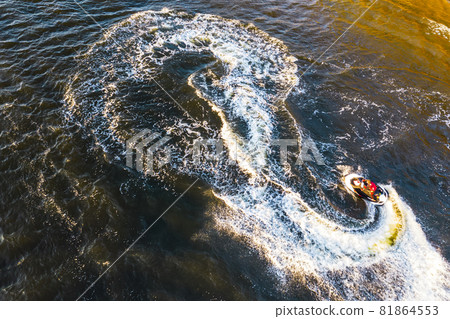 Aerial view of Young man making infinite loop riding on fast water scooter on sunset in Golden water. Drone photo of tourist having fun riding a water bike doing eight sign on the sea with pleasure Aerial view of Young man making infinite loop riding on fast water scooter on sunset in Golden water. Drone photo of tourist having fun riding a water bike doing eight sign on the sea with pleasure 81864553