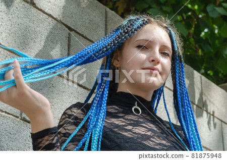 Young woman against gray stone wall. Lovely woman with long blue pigtails. Daytime. Selective Focus 81875948