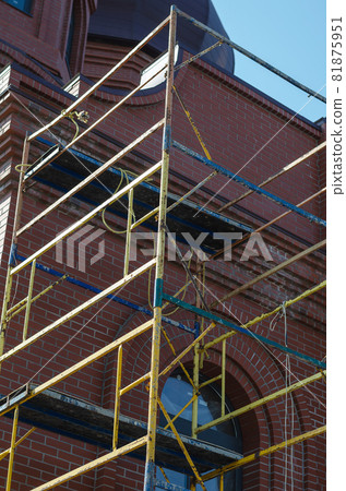 Yellow scaffolding in front of the red brick building. Construction Industry. Architecture. View from bottom to top. Yellow scaffolding in front of the red brick building. Construction Industry. Architecture. View from bottom to top. 81875951