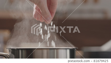 man adding salt to boiling water in saucepan 81879425