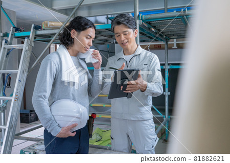 A site director and two carpenters talking while looking at a tablet at a construction site 81882621