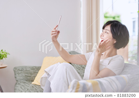 A young lady watching a smartphone on a sofa A young lady watching a smartphone on a sofa 81883200