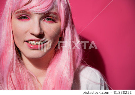 Close-up portrait of a young woman with braces in a pink wig on a pink background. 81888231