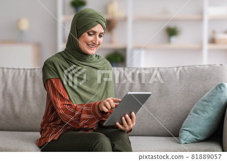 Muslim Lady Using Digital Tablet Browsing Internet Sitting At Home Muslim Lady Using Digital Tablet Browsing Internet Sitting At Home 81889057