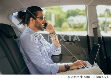 Positive arab man freelancer working online while sitting in taxi Positive arab man freelancer working online while sitting in taxi 81889071