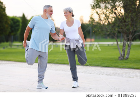 Smiling senior man and woman doing legs stretching exercises helping each other by holding hands Smiling senior man and woman doing legs stretching exercises helping each other by holding hands 81889255
