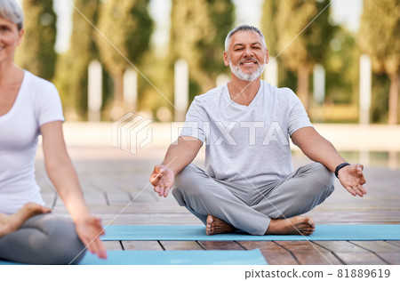 Happy senior husband and wife meditating with eyes closed in lotus position during yoga outdoors 81889619