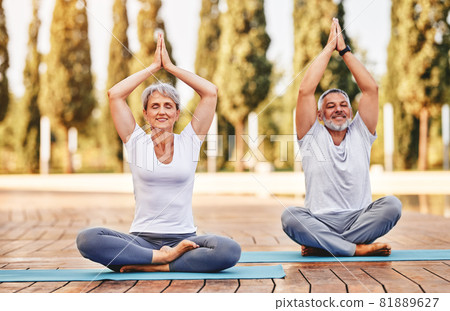 Happy senior husband and wife meditating with eyes closed in lotus position during yoga outdoors 81889627
