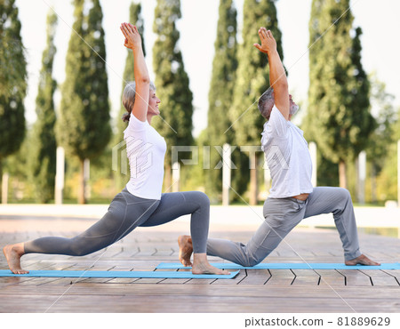 Fit mature couple senior woman and man standing barefoot in warrior Virabhadrasana pose outside Fit mature couple senior woman and man standing barefoot in warrior Virabhadrasana pose outside 81889629