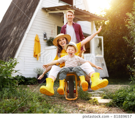 cheerful   family of farmers enjoying   holiday  and having fun. mother and father roll their kid boy in a garden wheelbarrow in the summer 81889657