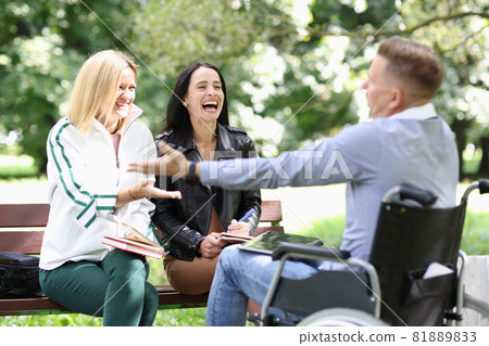Disabled man in wheelchair communicating and laughing with women in park Disabled man in wheelchair communicating and laughing with women in park 81889833