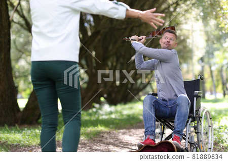 Disabled man in wheelchair is swinging violin at woman in park Disabled man in wheelchair is swinging violin at woman in park 81889834