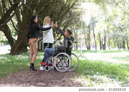 Disabled man in wheelchair giving five to female friends in park Disabled man in wheelchair giving five to female friends in park 81889838